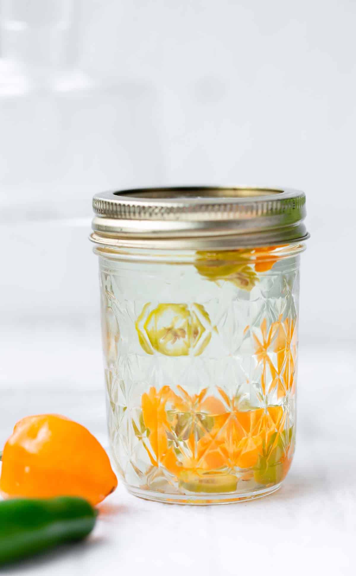 Close up of a jar of clear tequila with sliced chilies inside.