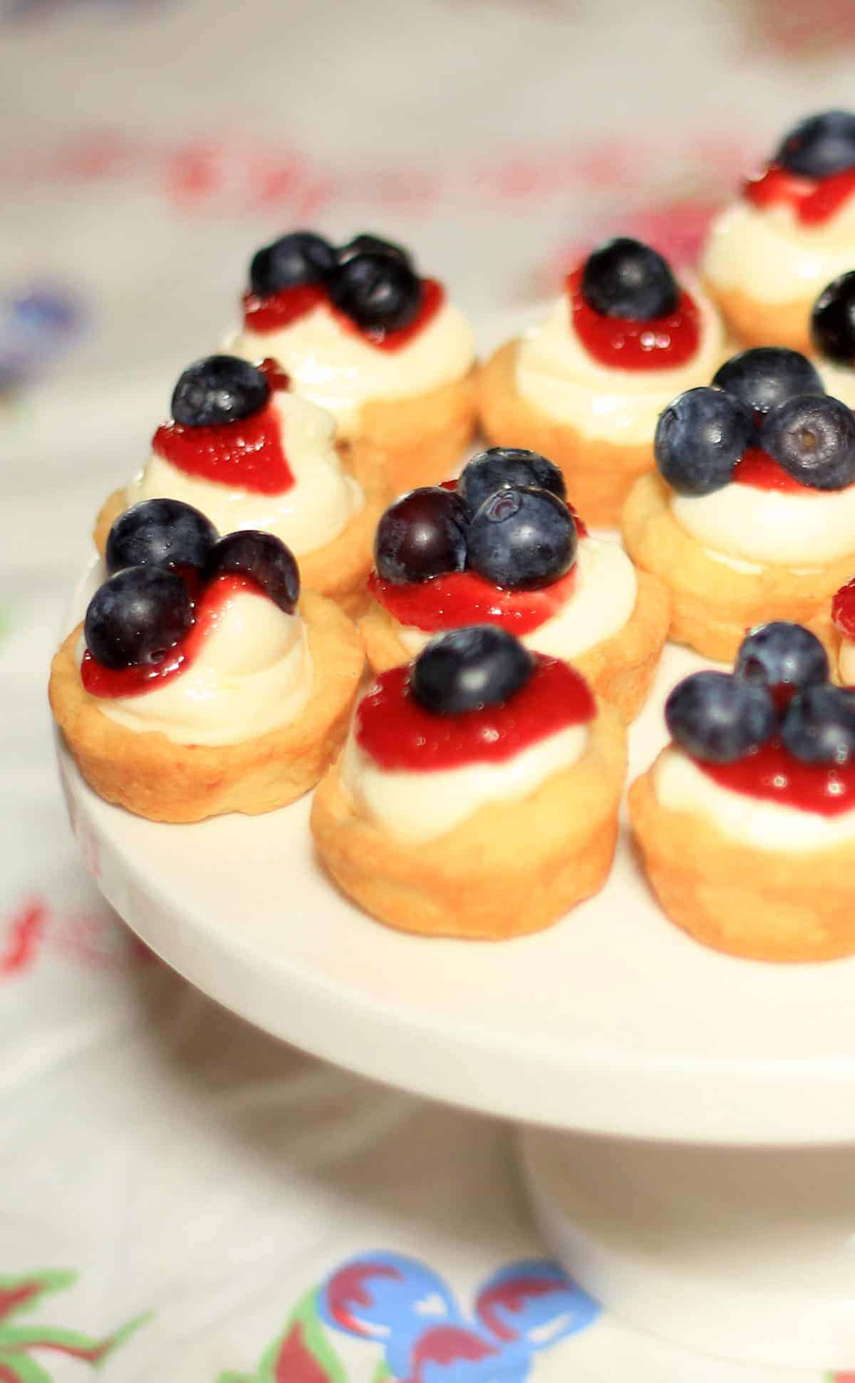 Mini Red White and Blue Lemon Cheesecake Tarts are tender homemade lemon tart shells filled with no bake lemon cheesecake filling then finished with a topping of sweet jam and berries. no bake cheesecake tarts | lemon cheesecake recipe | fruit tarts