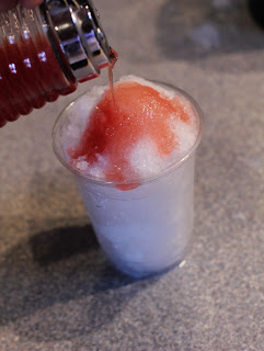 a cup of shaved ice with watermelon syrup being poured over the top