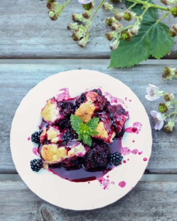 Blackberry cobbler with fresh blackberry branches on a wood table.