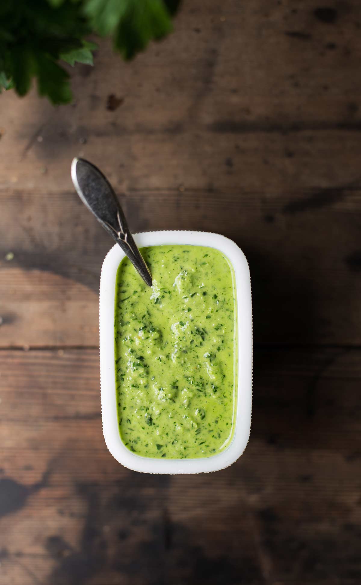 Bright green chimichurri sauce in a vintage white dish with spoon on wood background