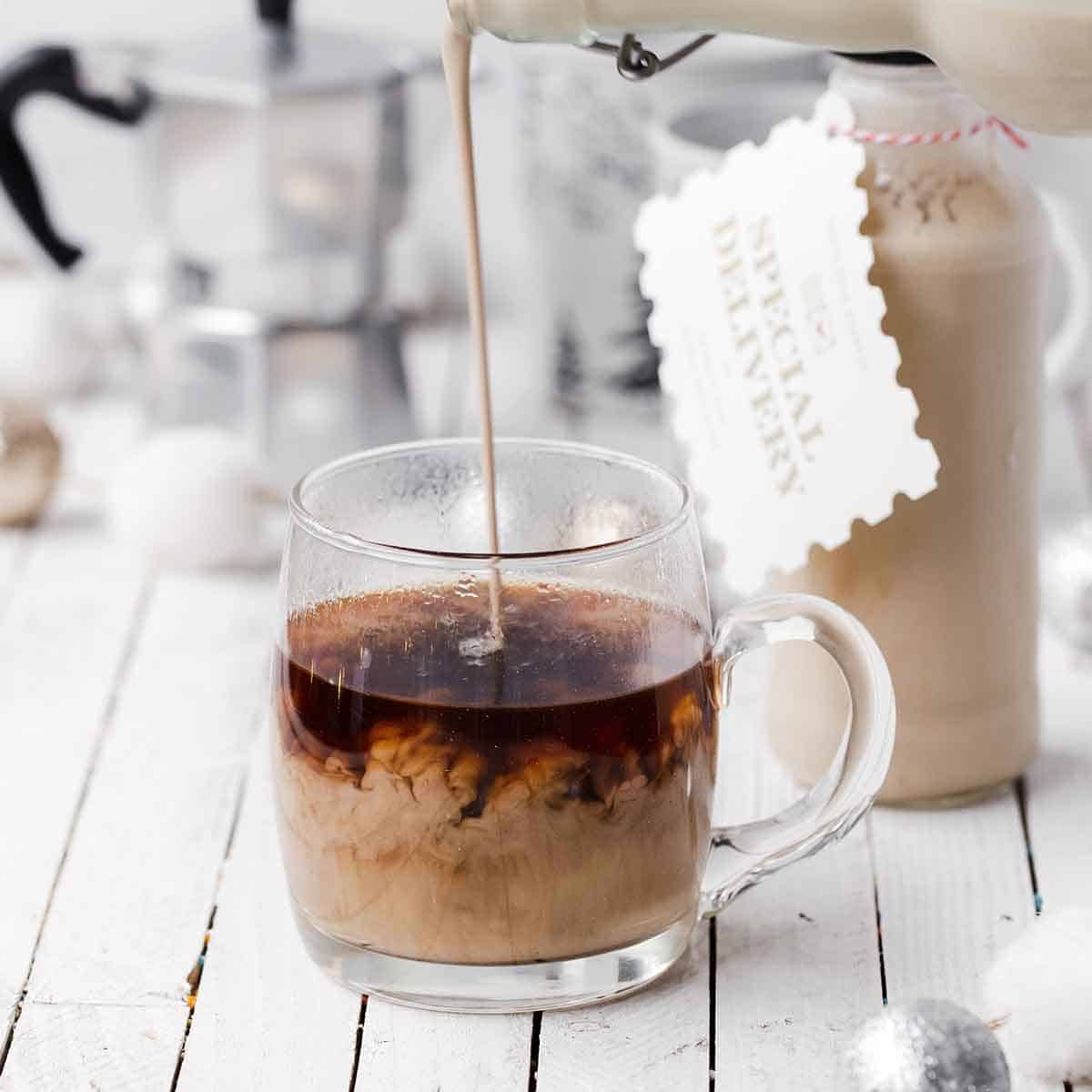 Homemade Baileys Irish Cream being poured into a glass coffee cup so that the swirls of dark coffee and light cream are visible.