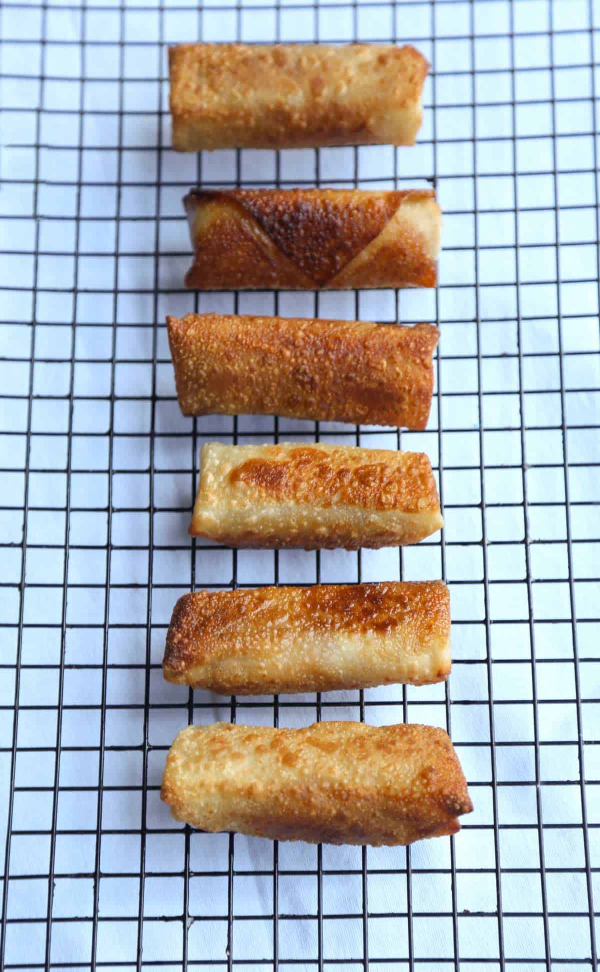 Crispy bubbly brown fried banana egg rolls on a cooling rack.