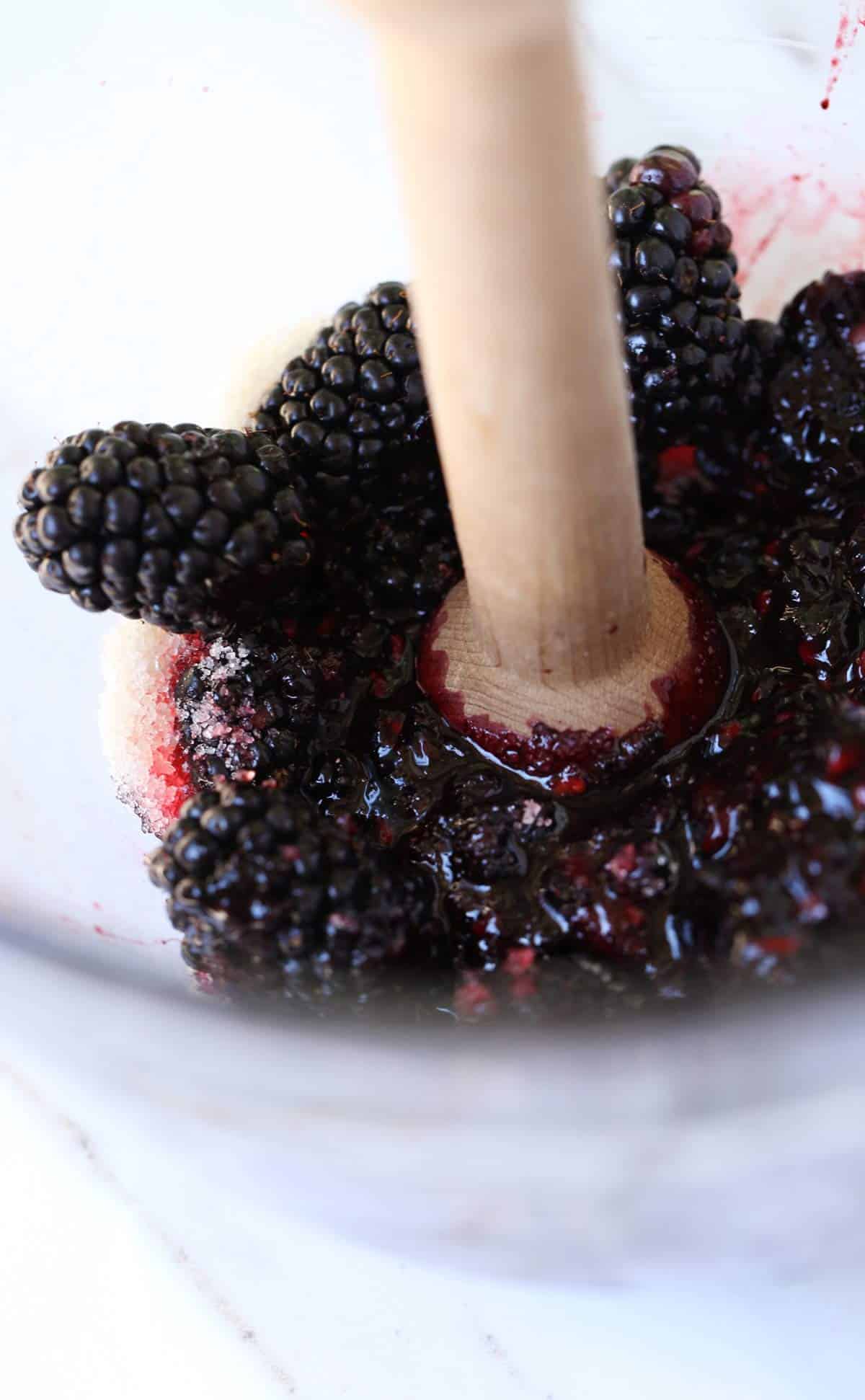 Blackberries and sugar being smashed into a jam like mixture