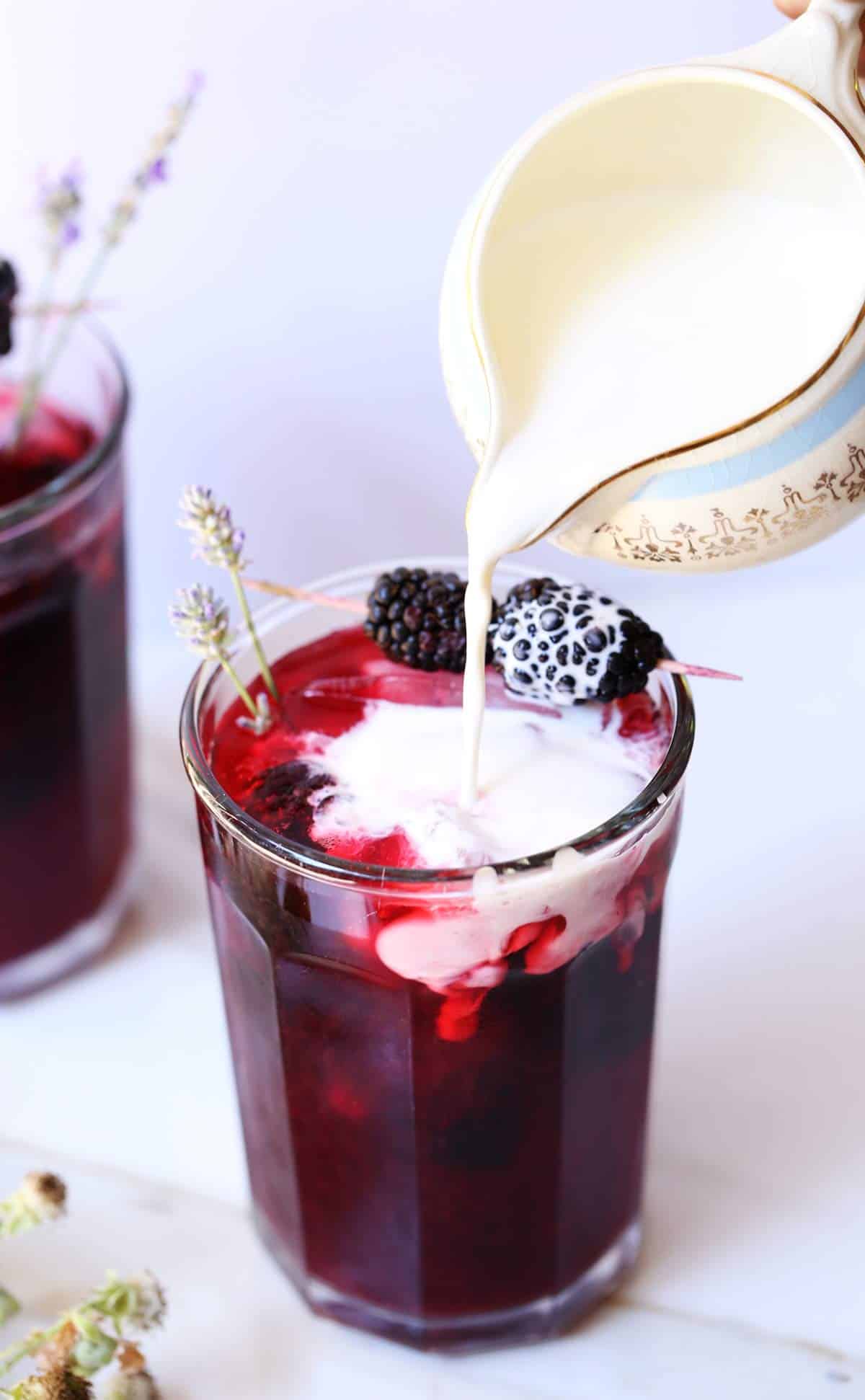 Cafe glass with bright purple blackberry tea with cream garnished with lavender and blackberries.