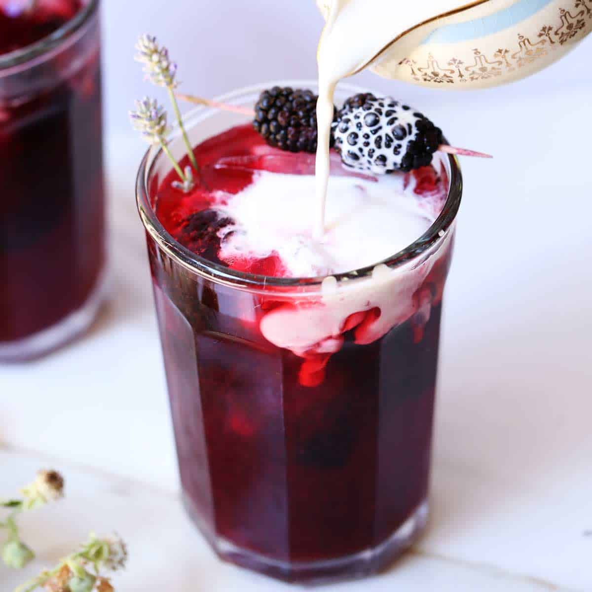 Bright purple blackberry iced tea with cream garnished with lavender and fresh blackberries