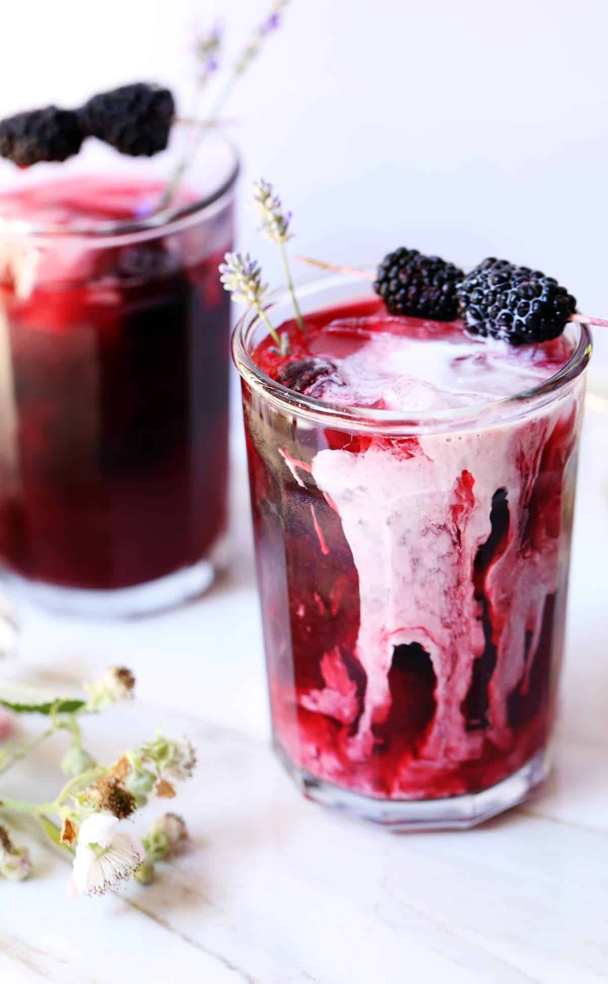 Blackberry tea with cream cascading in swirls down the side of the glass and fresh blackberries and lavender.