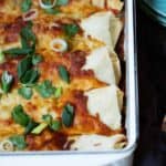 Chile verde chicken enchiladas made with flour tortillas covered in melted cheese with scallion and cilantro garnish.