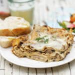 A slice of vegetable lasagna with parsley garnish and sweet tea in the background.