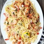 Shrimp scampi recipe made with gluten free pasta, lemon, garlic and herbs. Served on a platter with large pieces of lemon tossed into the pasta.