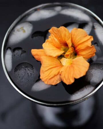 This delicious black halloween cocktail made with fresh mango and charcoal powder is delicious and stunning when garnished with a bright orange edible flower like nasturtium blossoms.