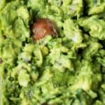Close up of homemade guacamole recipe with lime and cumin shown with the avocado pit in to maintain freshness and prevent browning.