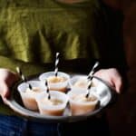 A tray of apple cider slushies in mini cups with black and white striped straws.