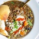 French green lentils stewed with vegetables served in a white bowl with a rustic loaf of bread.