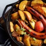 Smoked sausage and apples skillet meals in a cast iron pan garnished with fresh oregano.