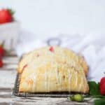 Strawberry lemon hand pies with icing drizzle stacked in a row with fresh strawberries to the side.