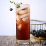Blueberry switchel drink on ice in a tall glass garnished with fresh blueberries.
