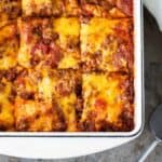 Baked taco lasagna in a casserole dish with melted cheddar cheese and flavorful ground beef.