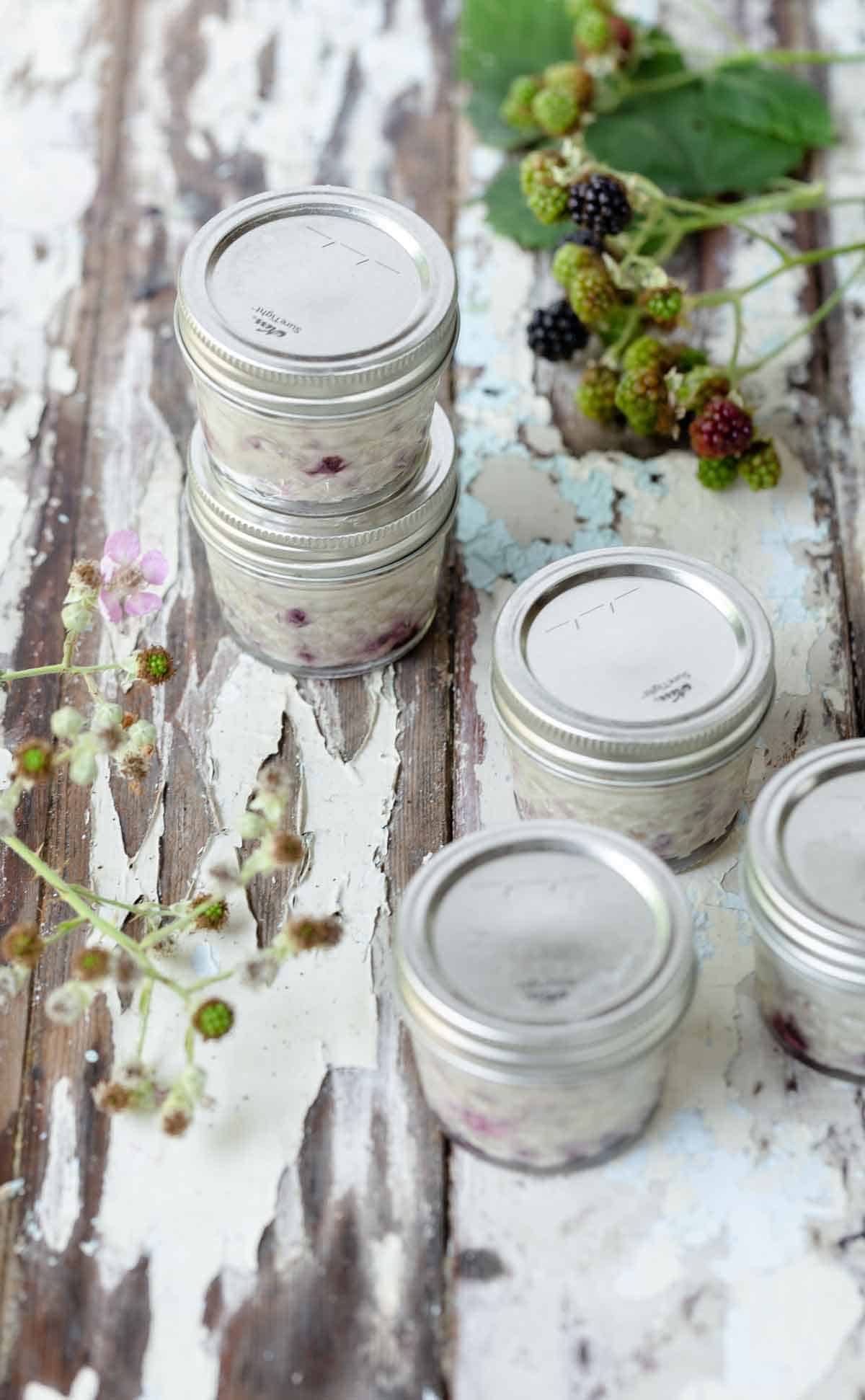 Blackberry creme brulee in jars with fresh berries around the sides.