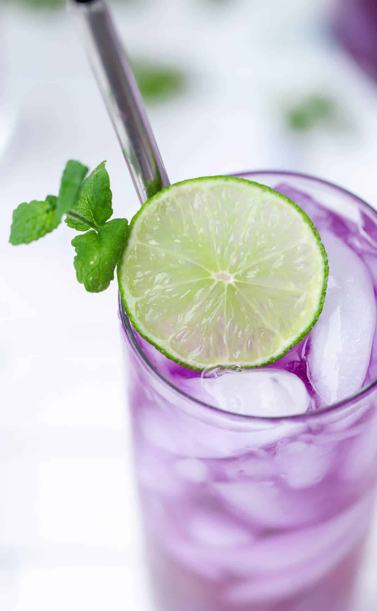 Top down view of butterfly pea flower cocktail with lime round and mint.