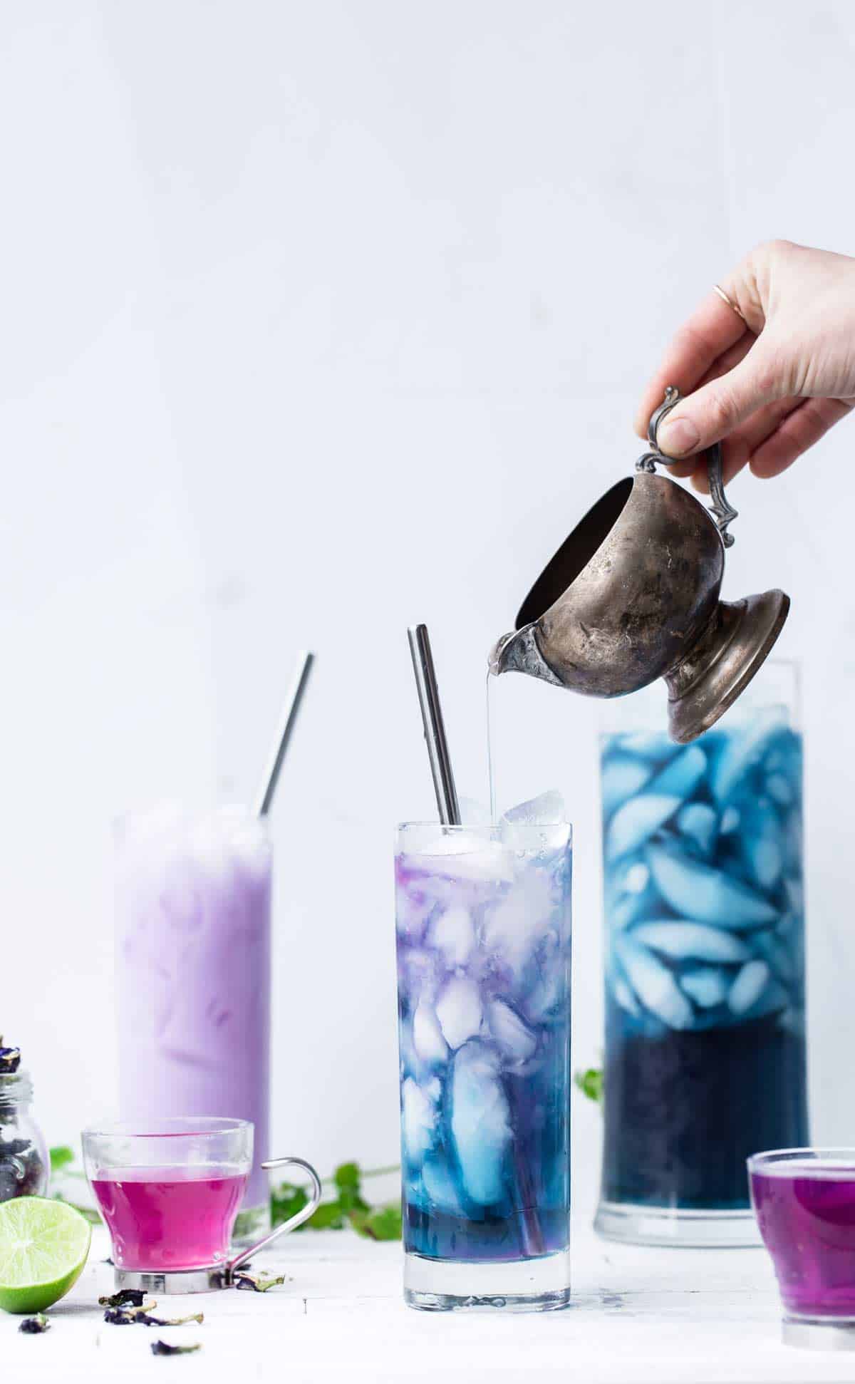 Butterfly pea tea with ice in a tall glass with lime juice being poured in and the tea changing color from blue to purple where the lime juice drizzles.