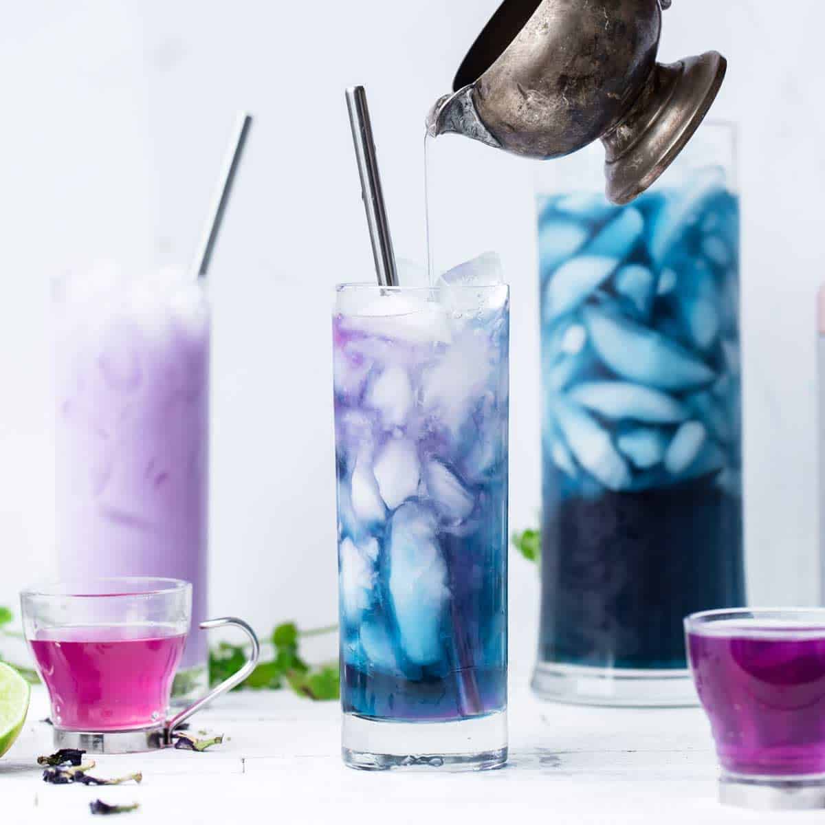 Color changing butterfly pea cocktail in a tall ice filled glass with lime juice being poured in changing the color into swirls of blue, pink and purple.