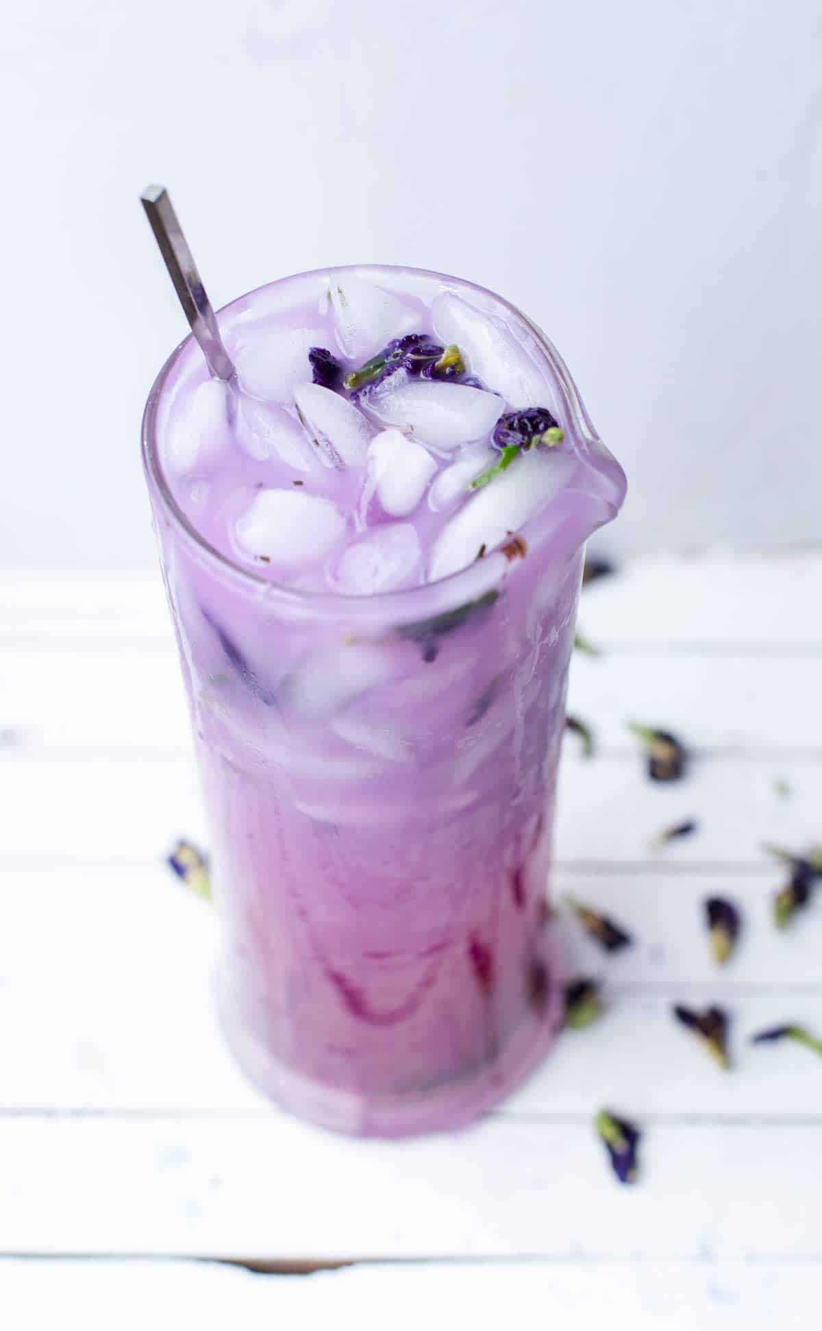 Big pitcher of purple iced tea with butterfly pea flowers scattered around.