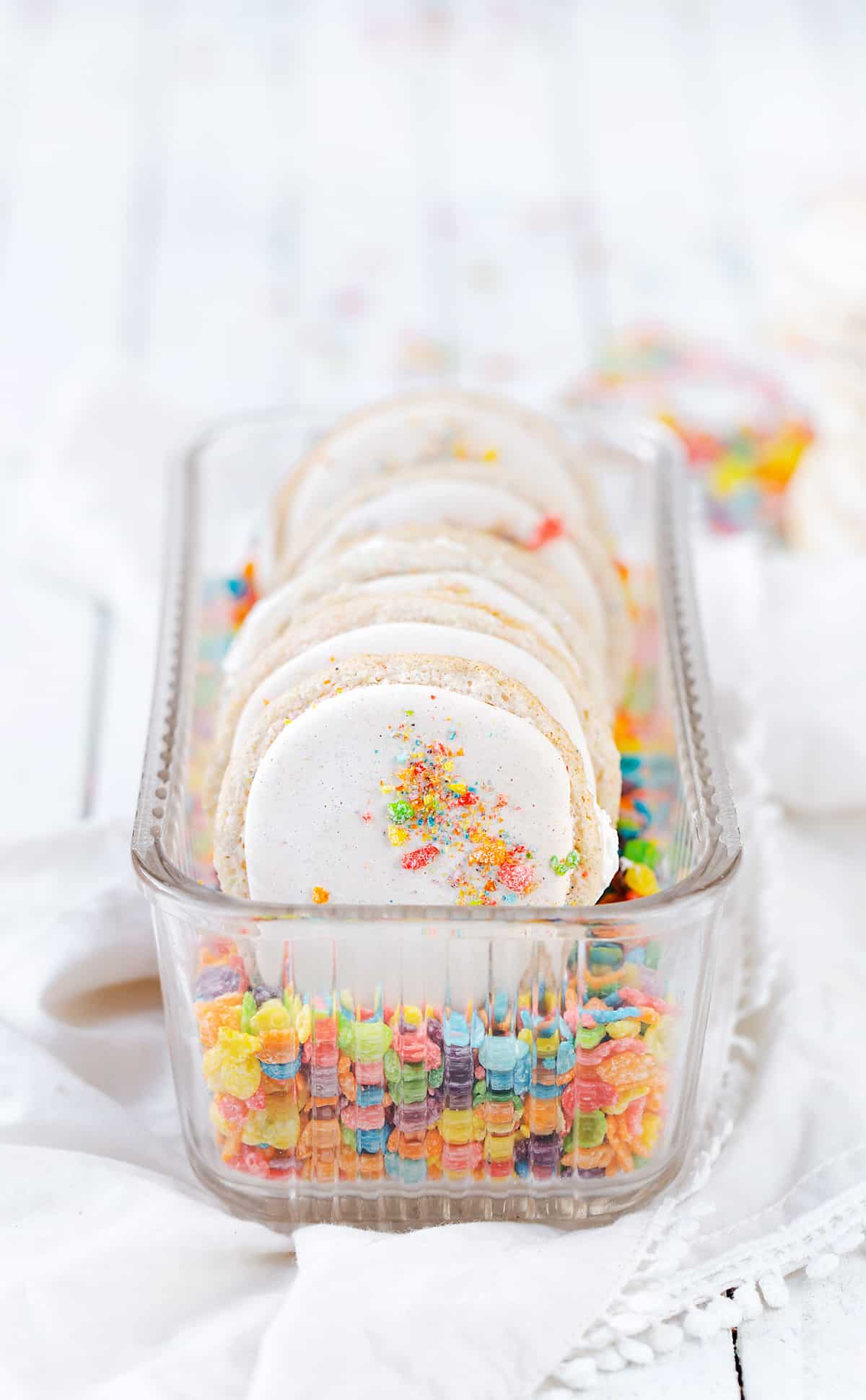 A vintage glass refrigerator dish filled with Fruity PEBBLES™ #ad cereal milk macarons and Fruity PEBBLES™ Cereal minimal food photography