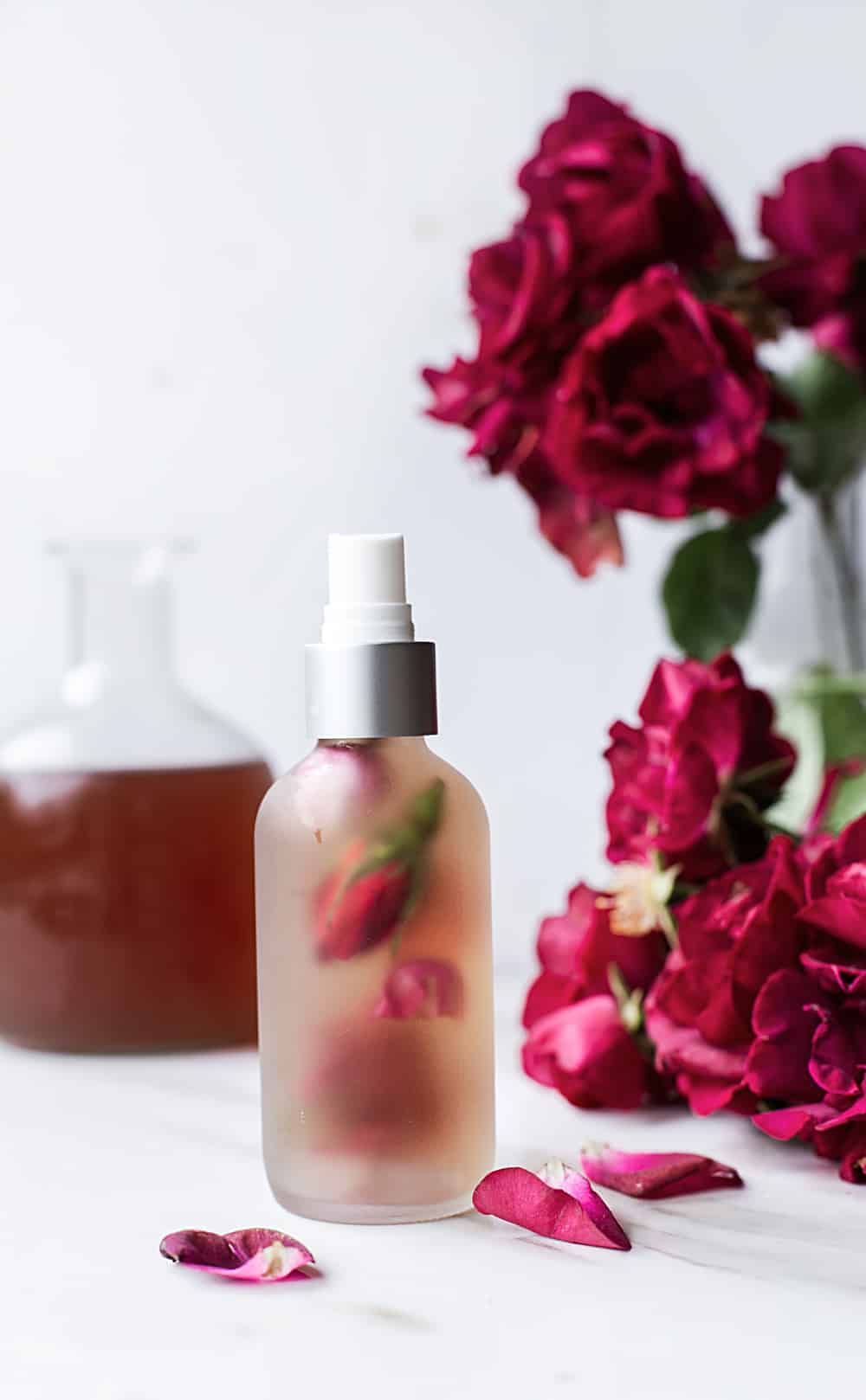 bottle of rose water with fresh roses and rose buds in the spray bottle