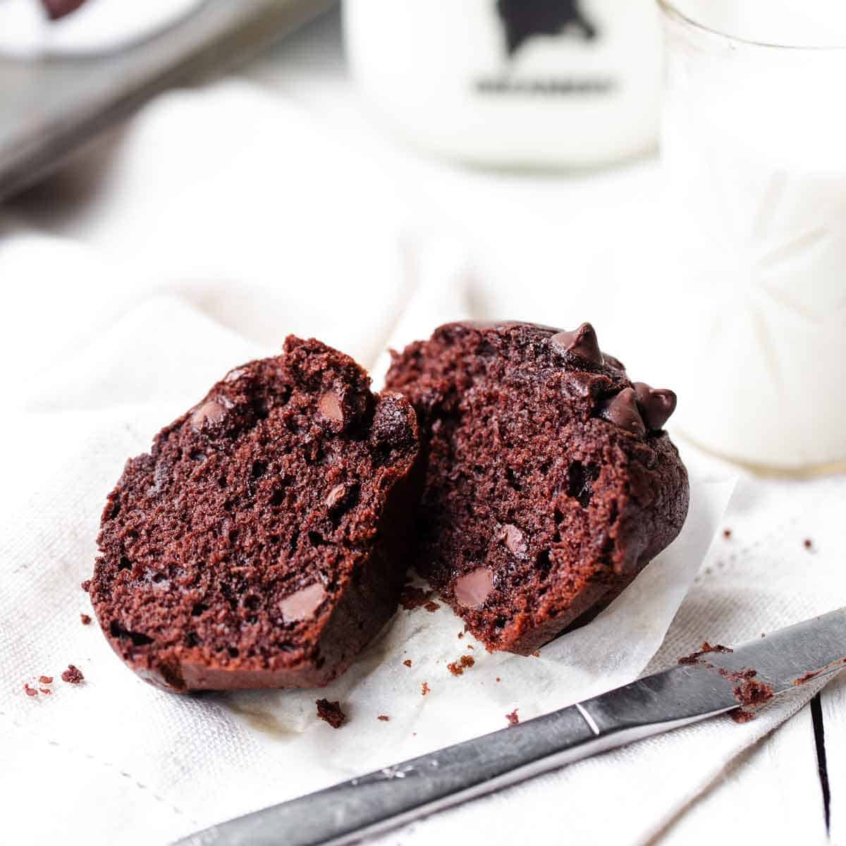 Moist double chocolate chip muffin cut in half with soft melted chocolate chips and a glass of milk in the background.