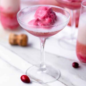 A scoop of cranberry apple sorbet in a coupe glass topped with a pour of sparkling wine.