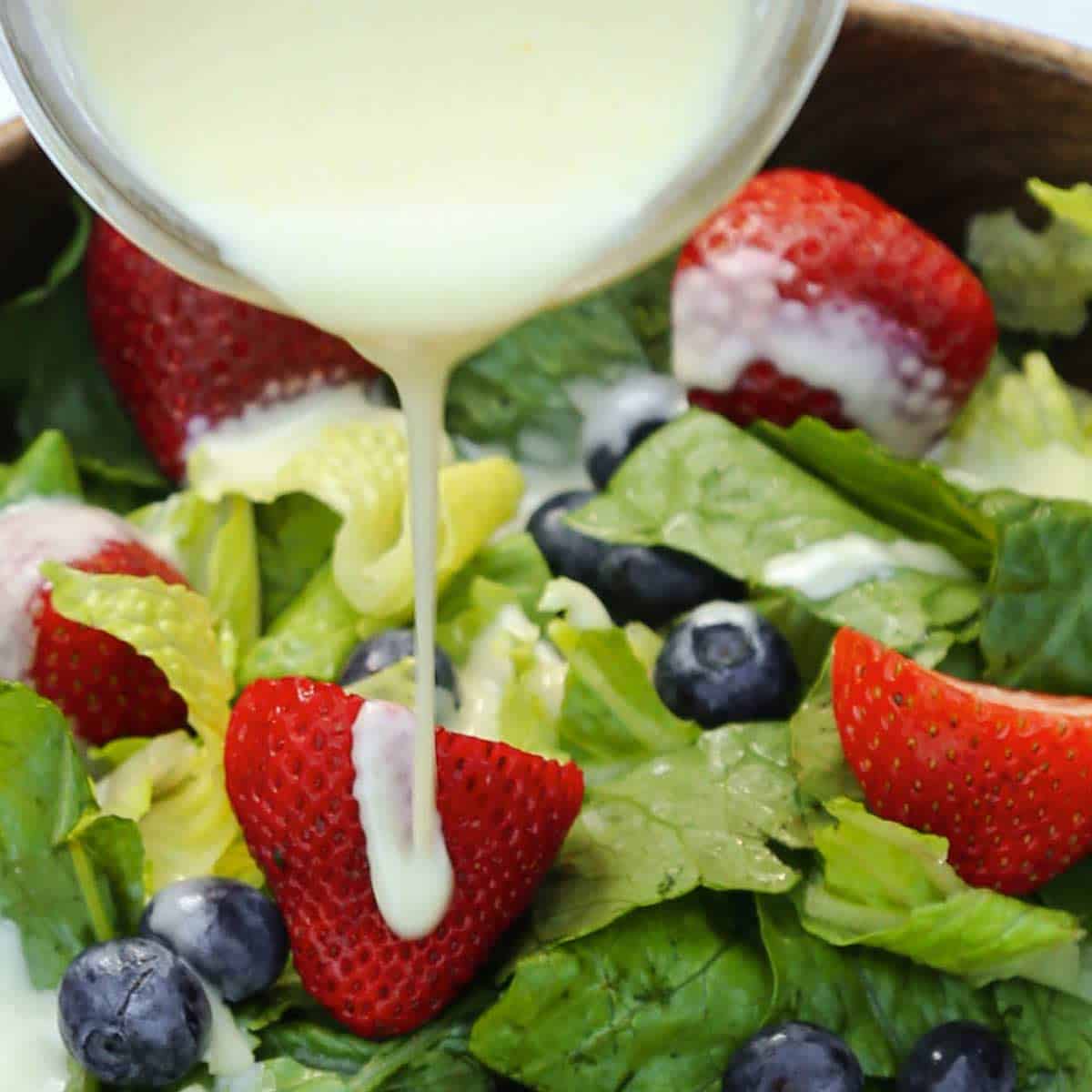 Lemon salad dressing being poured over a fresh green salad with strawberries and blueberries