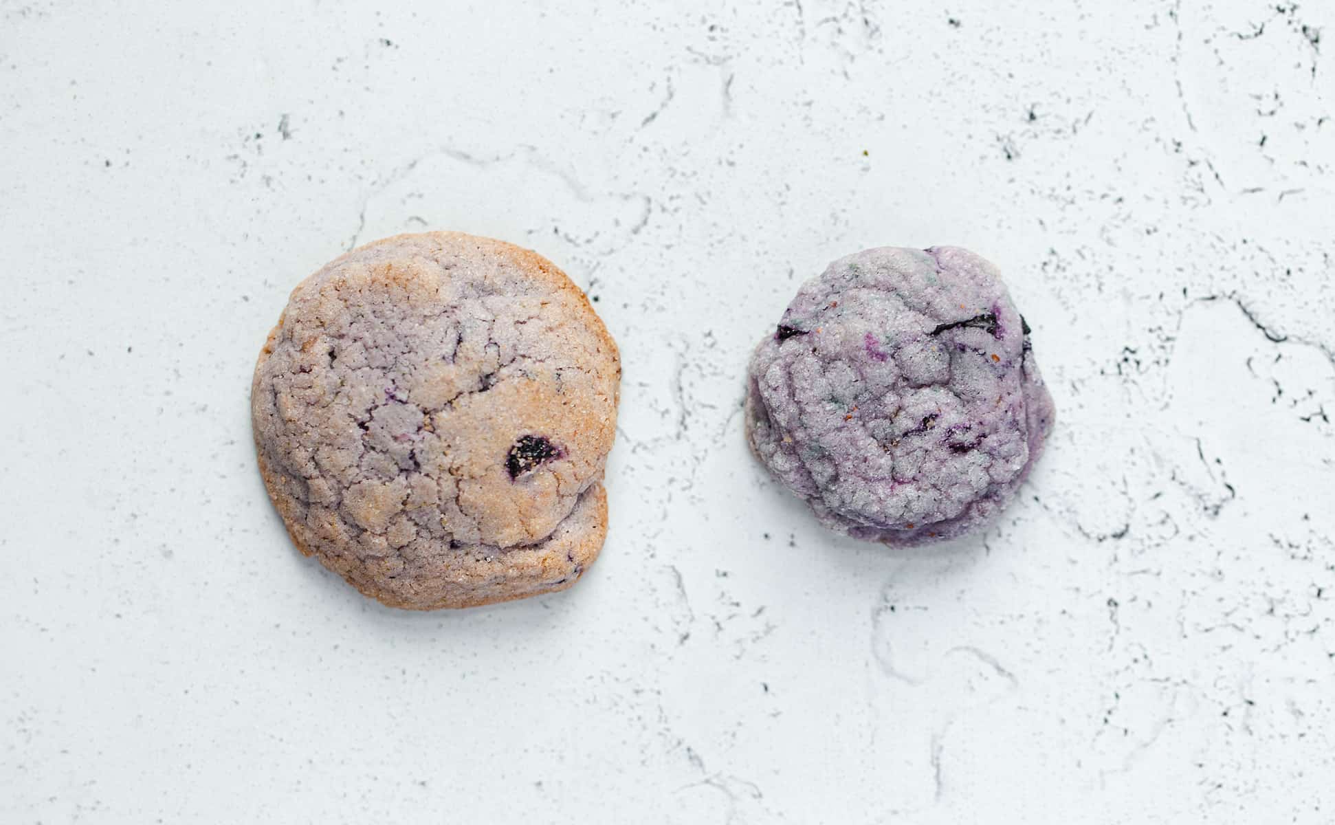 A vibrant purple blueberry cookie shown next to a dull brown over baked blueberry cookie.