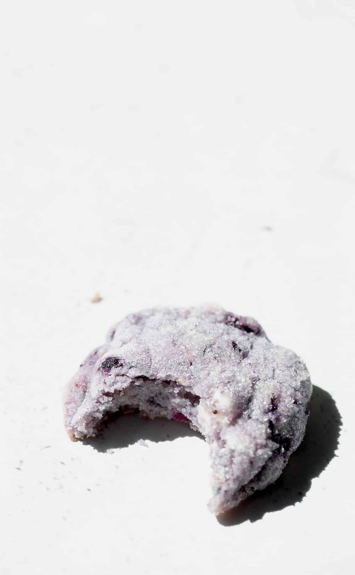 A close up of a super chewy blueberry cookie with a bite taken out of the middle.
