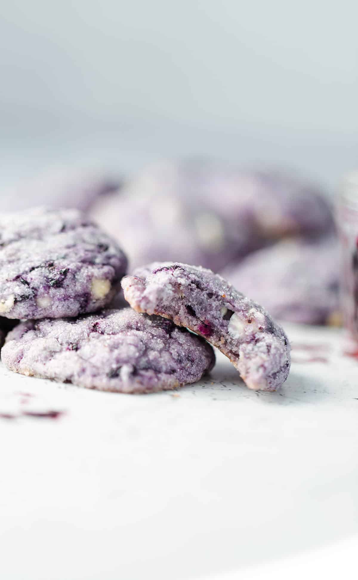 Chewy blueberry cookies stacked with a bite out of one so you can see the frozen blueberry pieces and white chocolate chips inside.