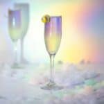 Color changing vodka cocktail made with butterfly pea vodka set against a hologram rainbow lighting effect with ice cubes all around.
