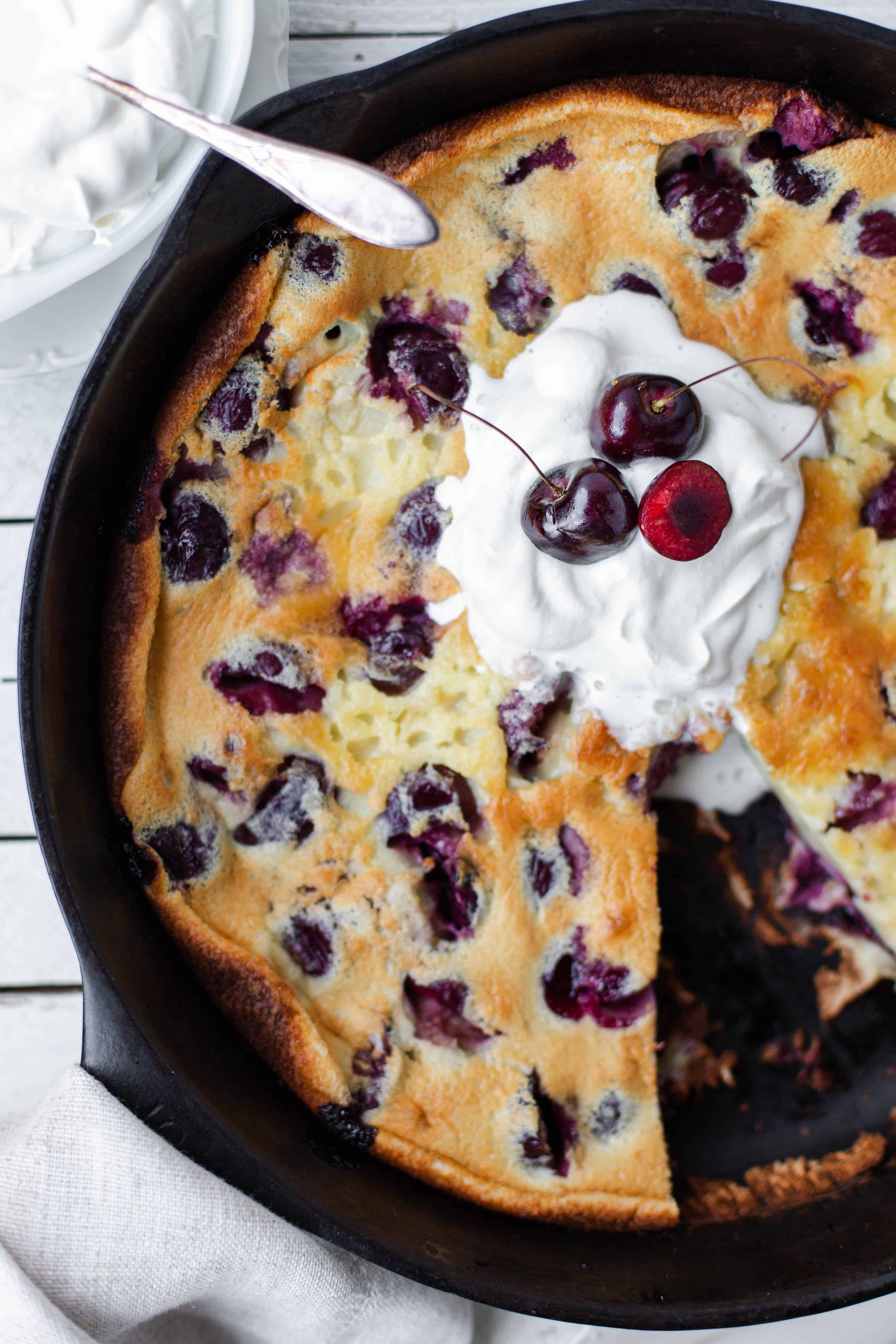 Top down view of cherry clafouti in a casti iron skillet topped with cherries.