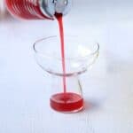 Homemade raspberry simple syrup pouring from a classic old fashioned syrup dispenser.