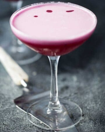A bright purple blueberry martini with a layer of luscious pink foam served on top of a vintage pie server.