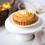 A mini tart shell with thin apple slices arranged on the top like a spiral rose.