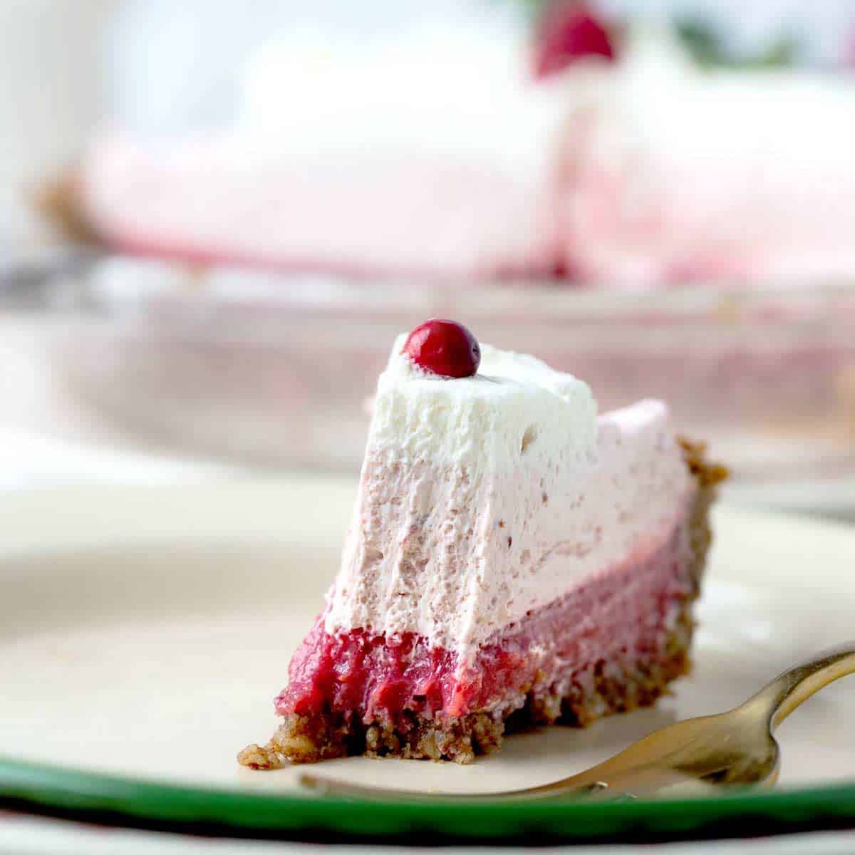 Cranberry pie with a bite out of it shows bright pink cranberry curd on the bottom, follow by light pink cranberry chantilly cream, then a thin layer of whipped cream.