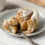 Gooey cinnamon roll on a plate with a fork showing a delicious bite of cinnamon roll.