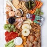 Top down view of a board full of snacks like pizza rolls, toaster strudels, fruit roll ups, celery sticks, pepperoni slices, crackers, peanut butter, pickles and more.
