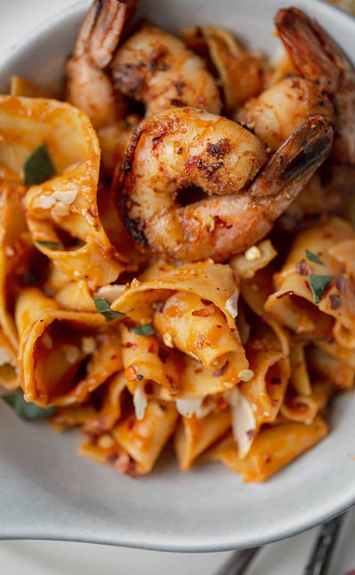 Close up of pan fried prawns with the tails on served with a large serving of red pepper pasta.