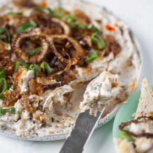 Three onion dip with green onion and vidalia onion and crispy onions on a plate with a knife and toast points.