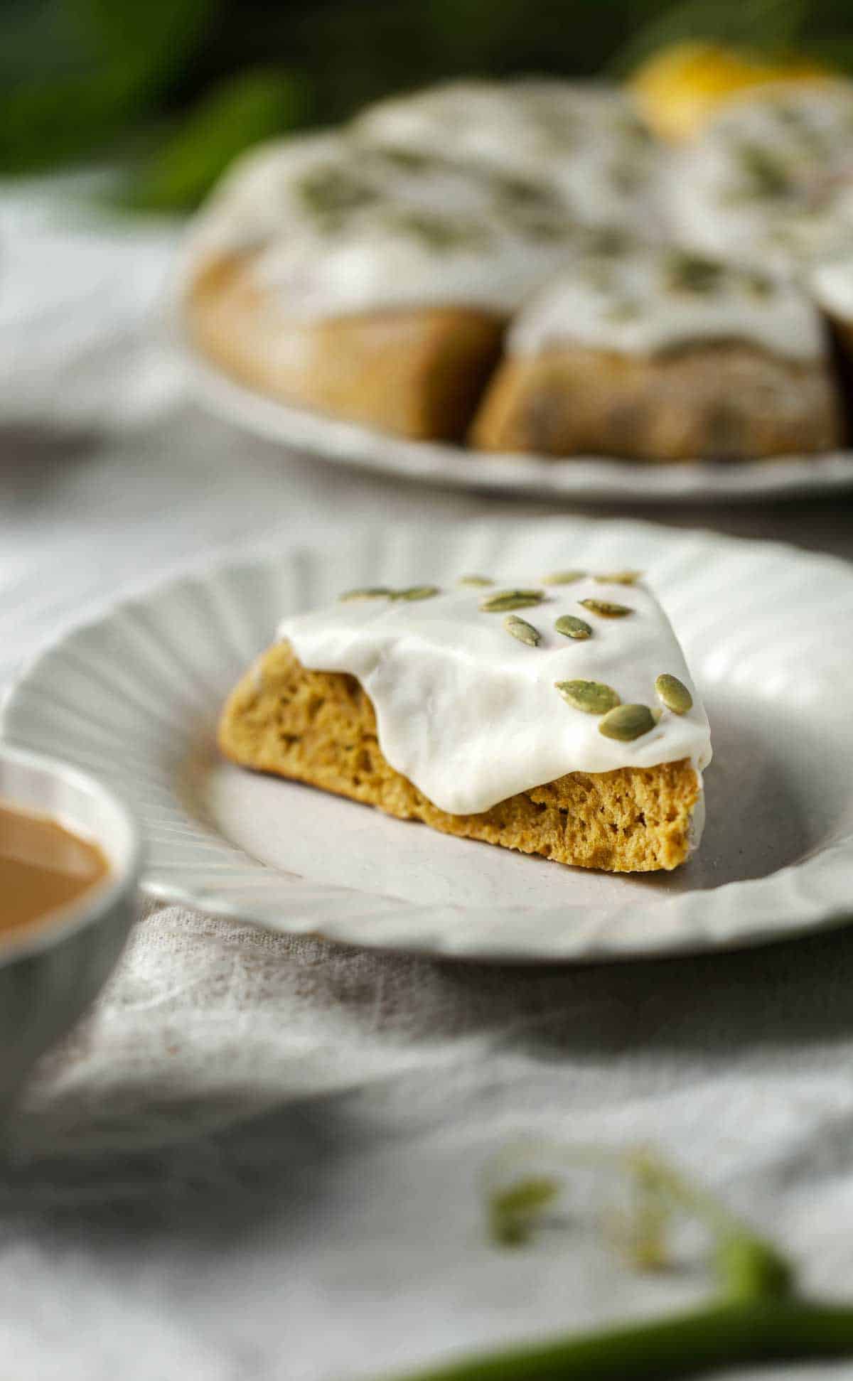 Soft fluffy pumpkin scone with thick glaze on a plate with pumpkin scones in the background.