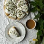 Pumpkin scones with thick glaze and pumpkin seeds from the top down with coffee cups and pumpkin vine off to the side.