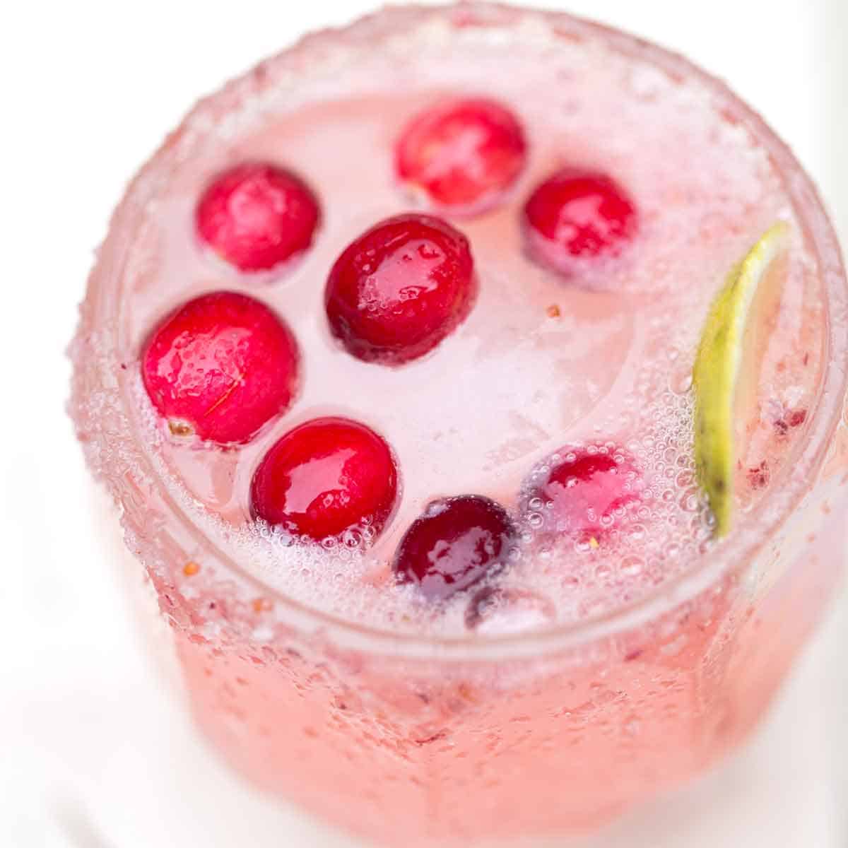 Fizzy pink cranberry paloma cocktail in a glass with fresh cranberries.