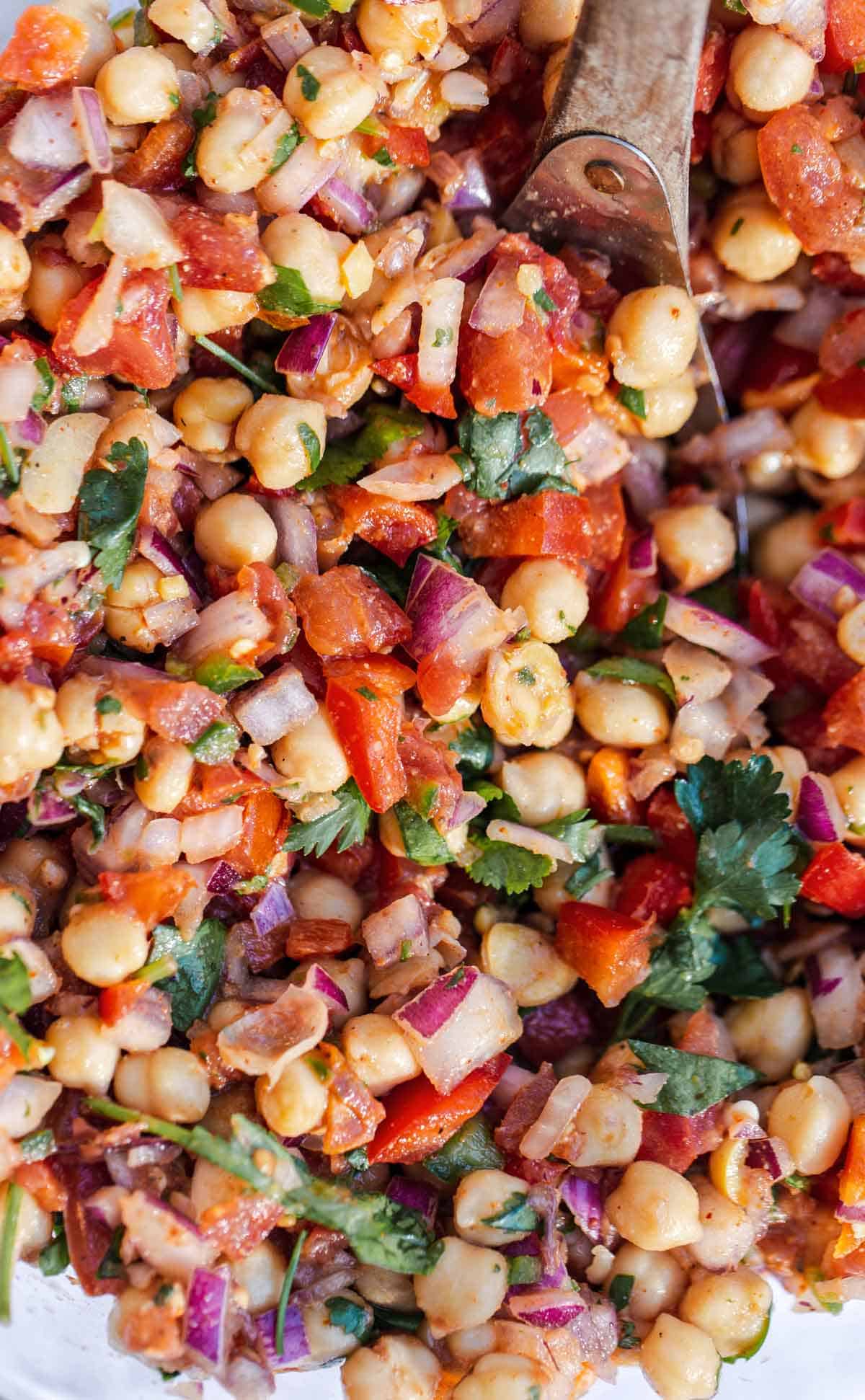 Indian salad with chickpeas and tomatoes in a bowl with a serving spoon.