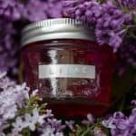 A jar of floral lilac jelly in a basket of fresh lilac flowers.